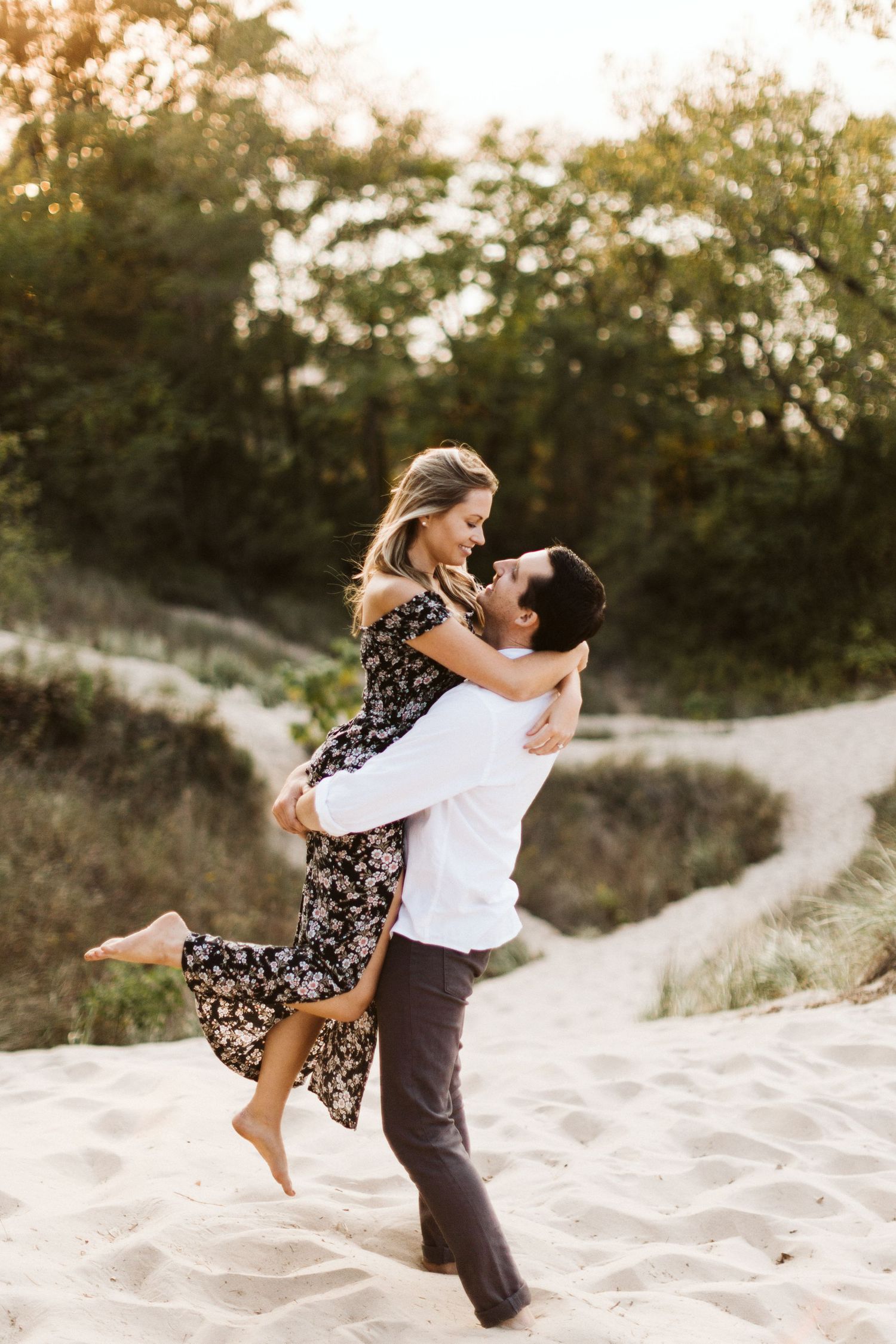 A couple plays and spins together on sandy dunes during a sunset photoshoot.