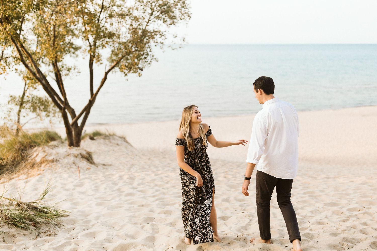 A couple walks together on a white sandy beach during sunset while holding hands and enjoying a romantic moment.
