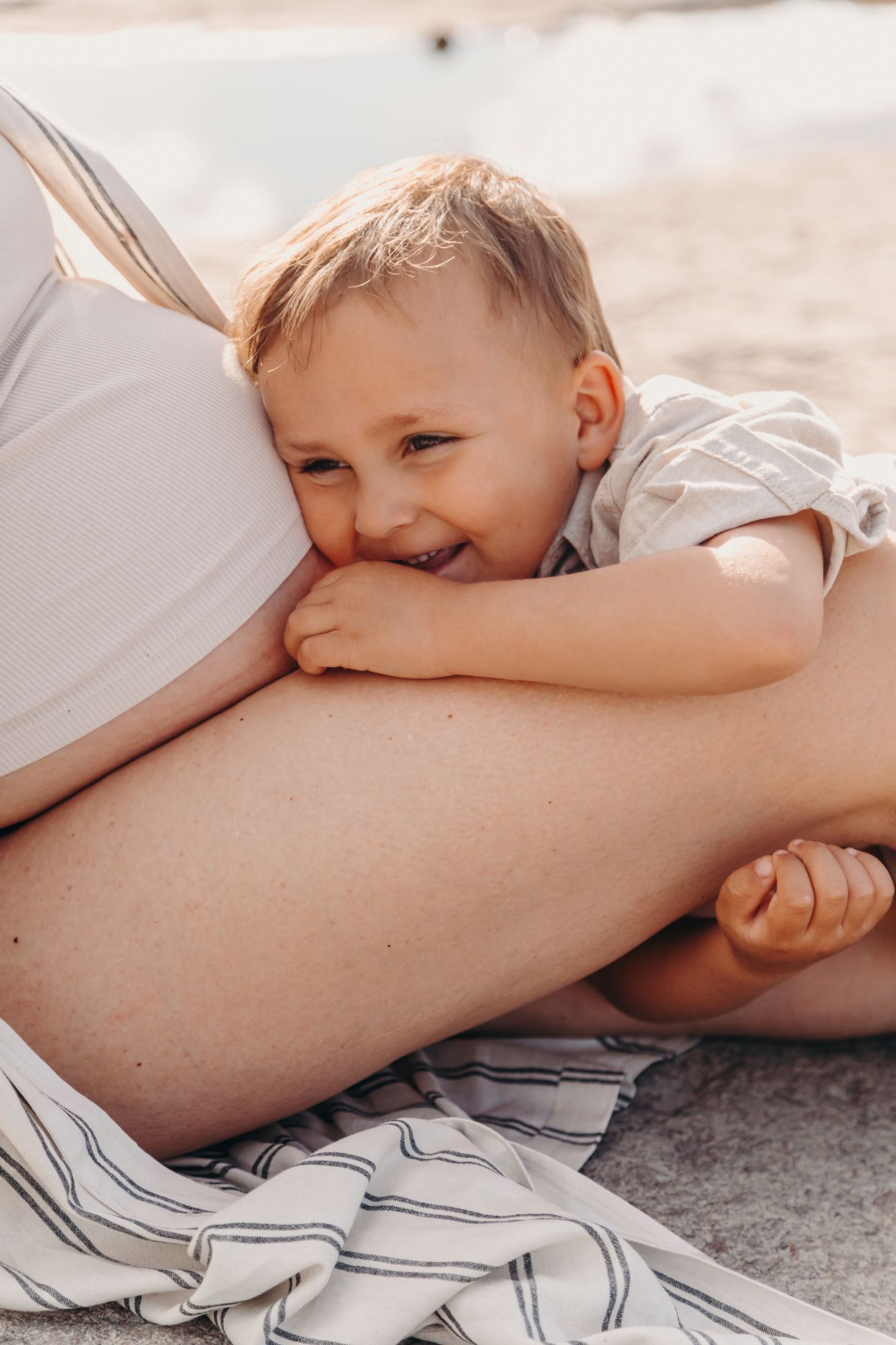 A small child giggles while resting on a blanket in warm sunlight during a tender family moment.
