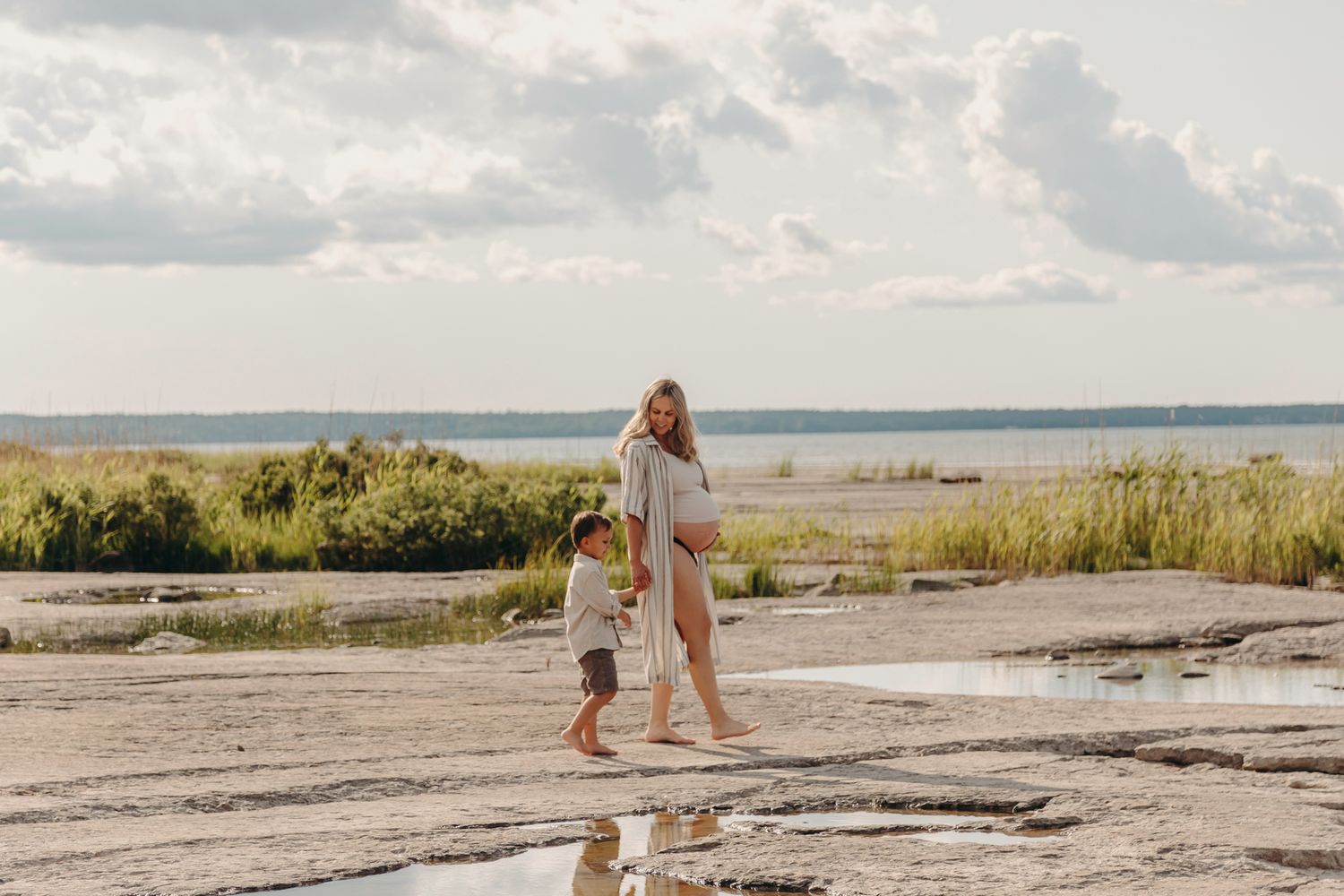 Family enjoys a summer day exploring rocky terrain along a scenic coastline with water and trees in the background.
