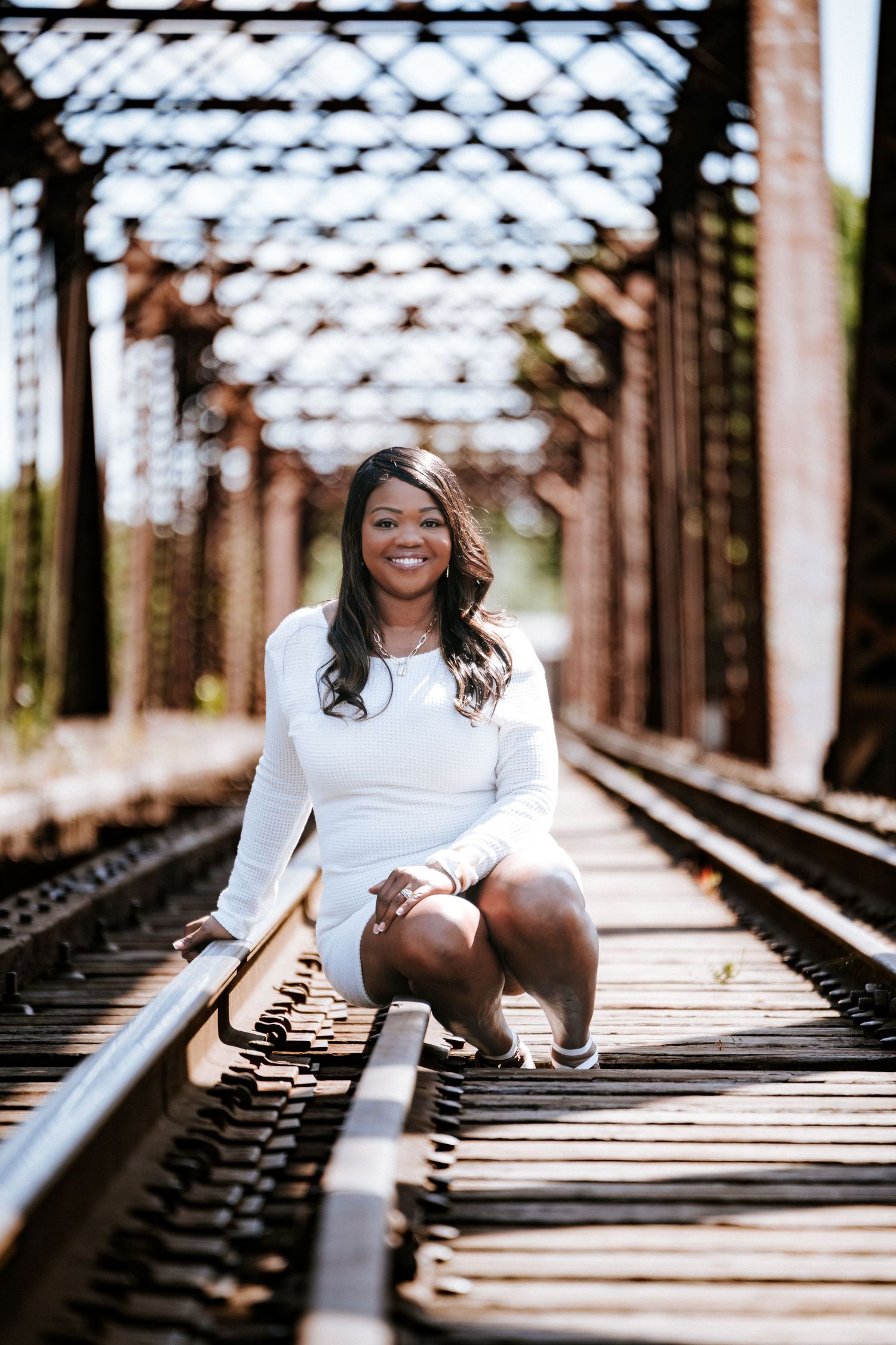 Artistic portrait series on railroad tracks with sunlight filtering through metal structure.