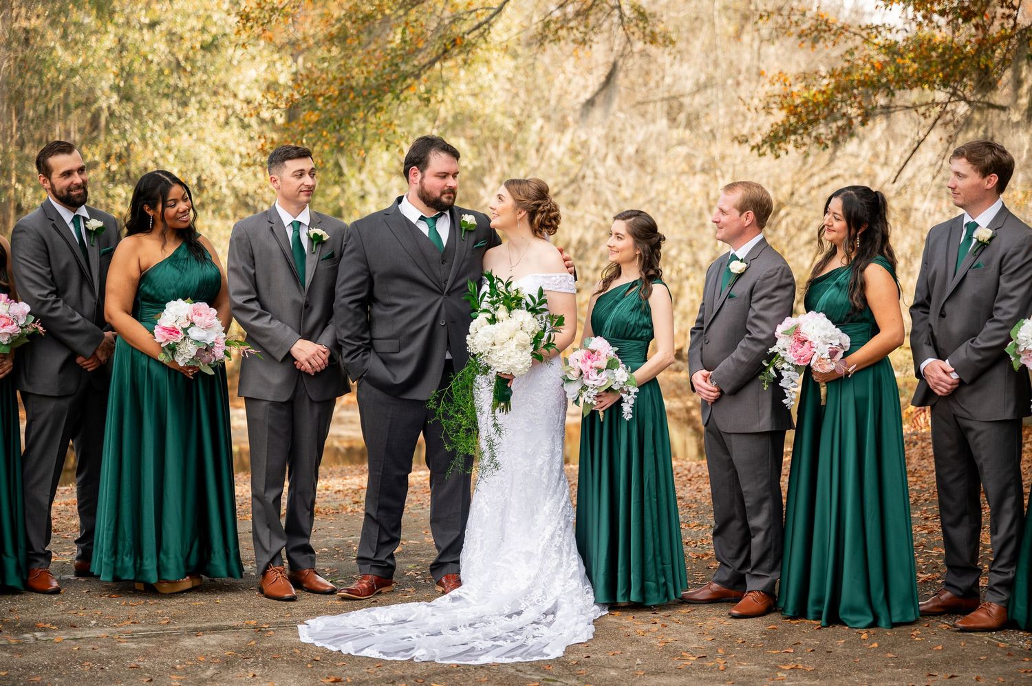 Wedding party members interact during outdoor photo session in autumn setting.