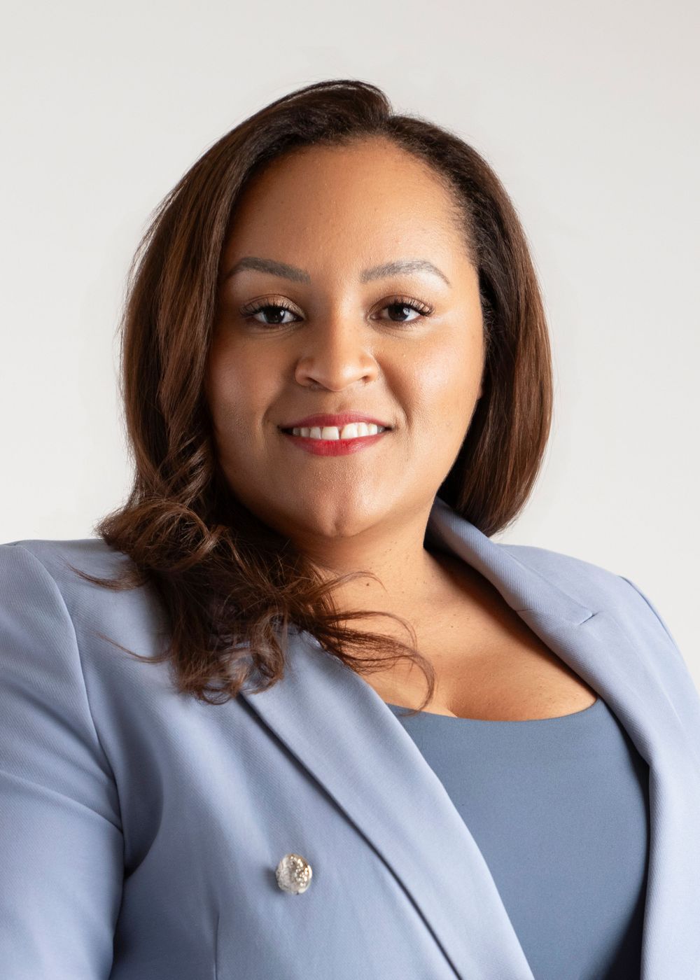 Professional headshot of someone in a light blue blazer smiling warmly against a neutral background.