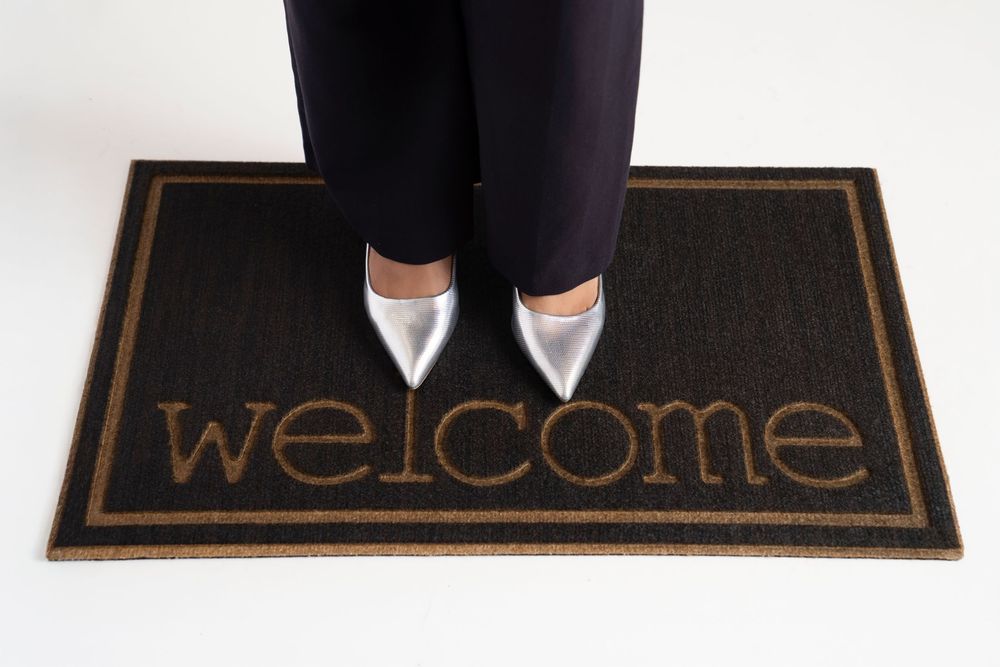 A black welcome doormat with white text sits at the entrance of a home.