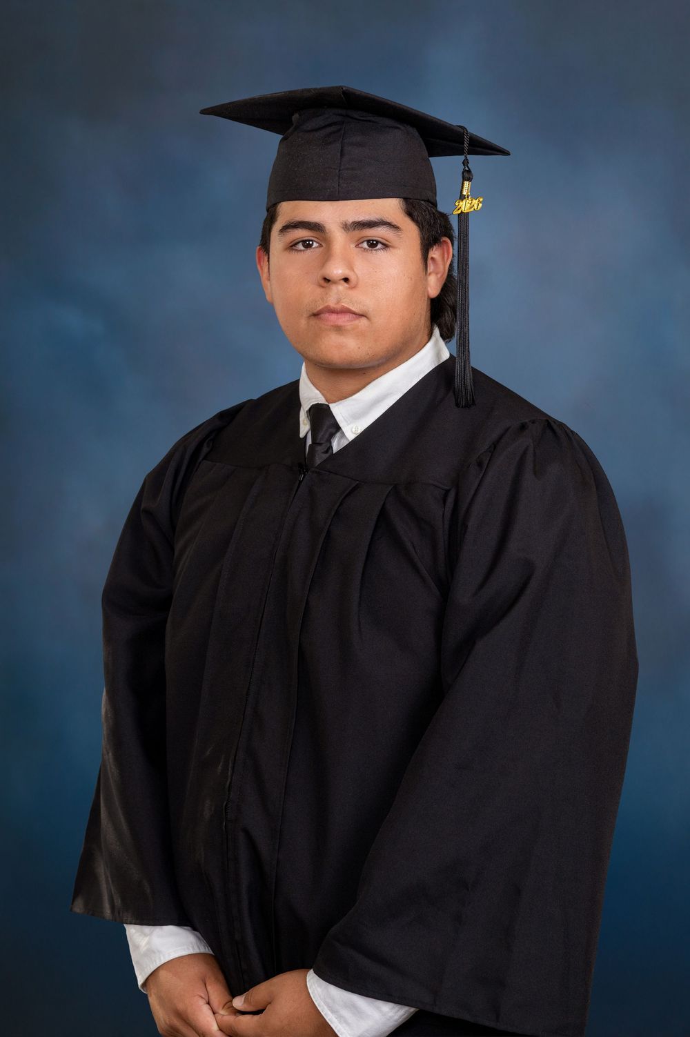 Graduate portrait session in traditional black cap and gown against blue backdrop.