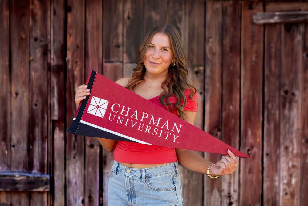 College student in casual attire poses with university banner against rustic wooden backdrop.