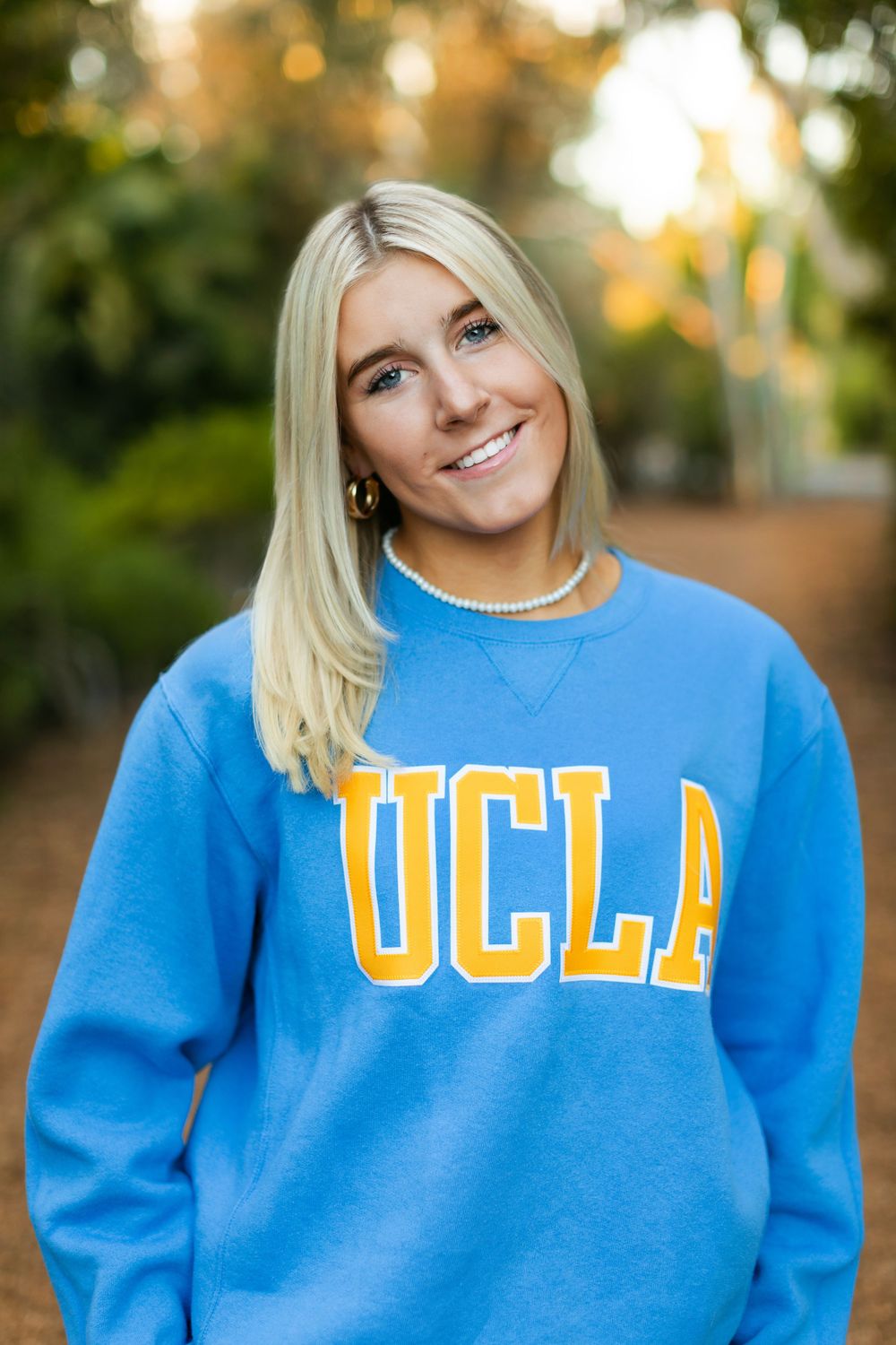 A series of photos showing someone in a bright blue UCLA sweatshirt posing outdoors with sunlit trees in the background.