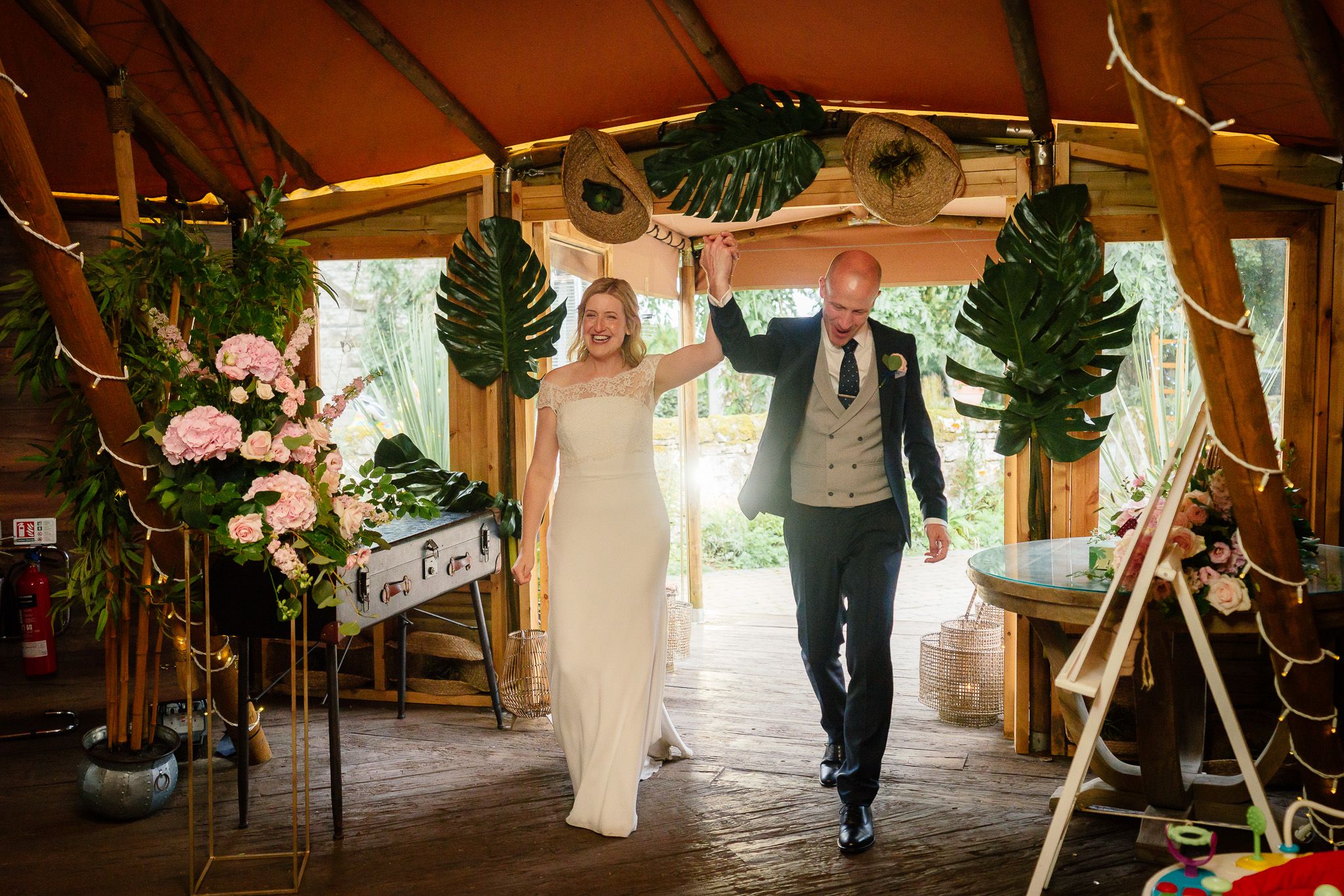 Wedding celebration in a rustic wooden venue decorated with tropical leaves and warm lighting. Woodhill Hall.