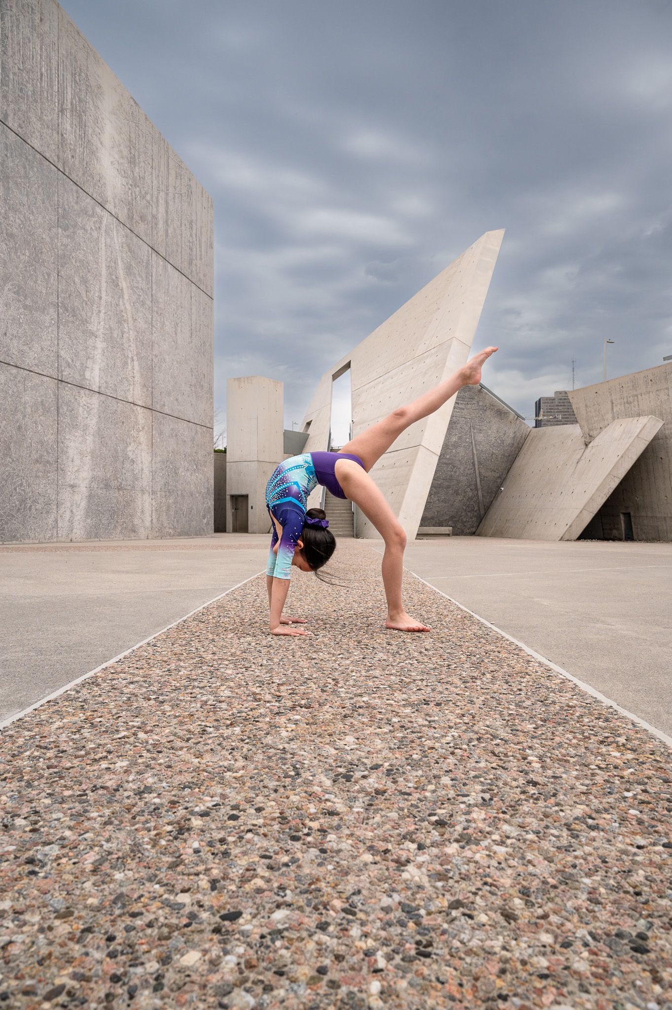 A sequence of parkour movements shows a person flipping and rolling across a concrete and gravel architectural space.