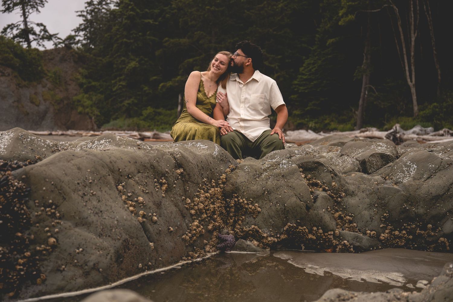 A embraces as they sit side by side on an Olympic National Park Beach at low tide.