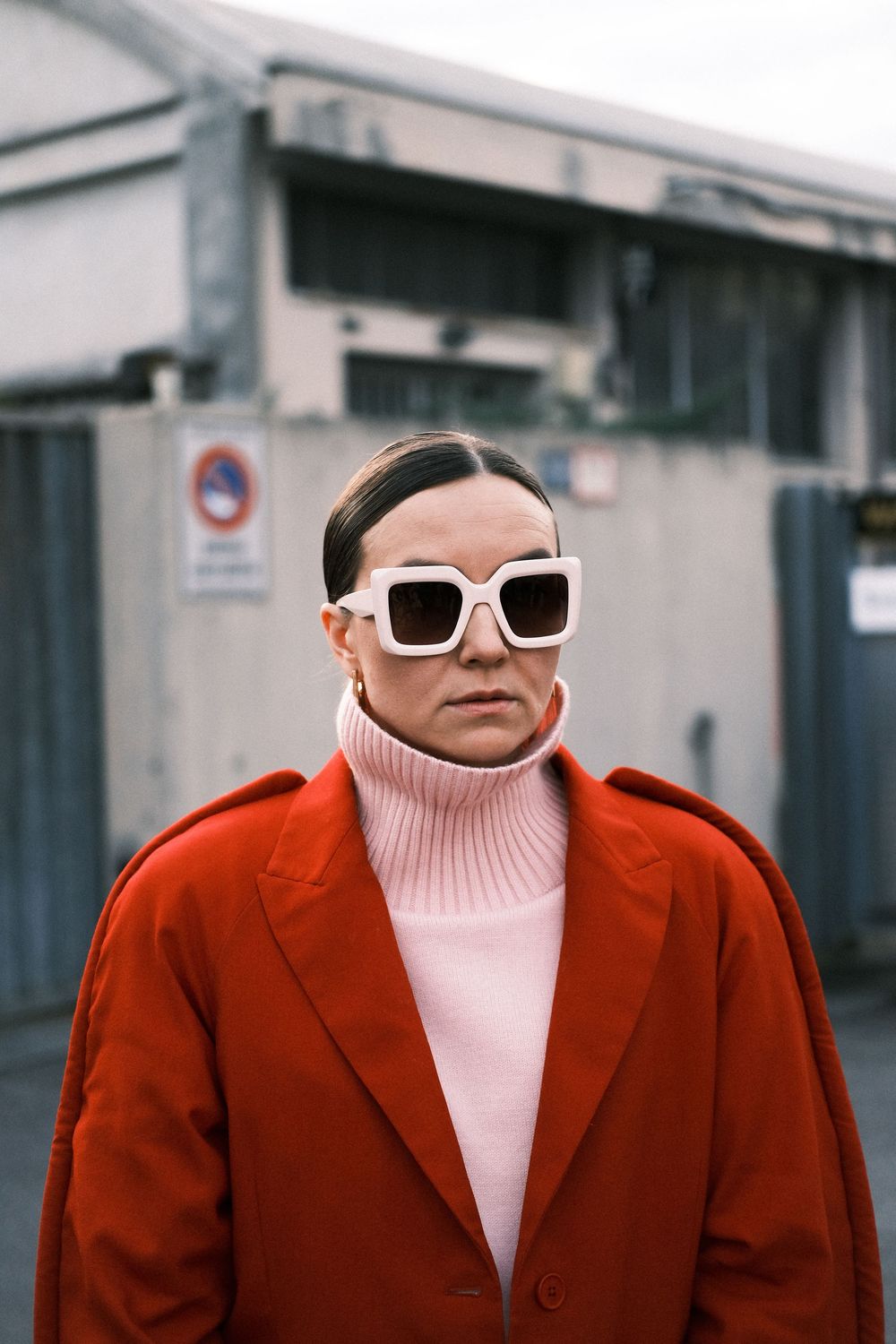 A person in a red blazer and pink turtleneck sweater wearing white sunglasses poses in a stylish street fashion look.