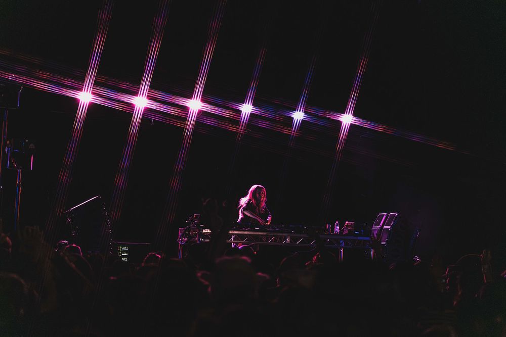 Pink and purple stage lights illuminate a dark concert venue with a dramatic lighting display.