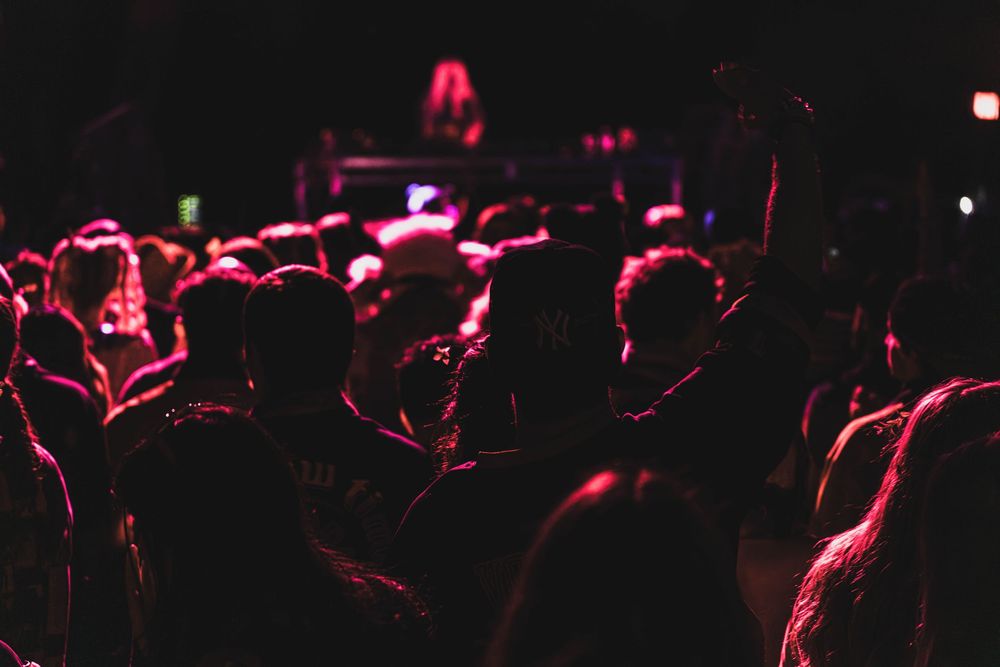 A crowd of silhouetted concert attendees illuminated by red stage lighting in a dark venue.