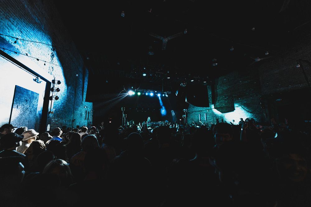 Concert crowd silhouettes against dramatic blue stage lighting at a nighttime music performance.