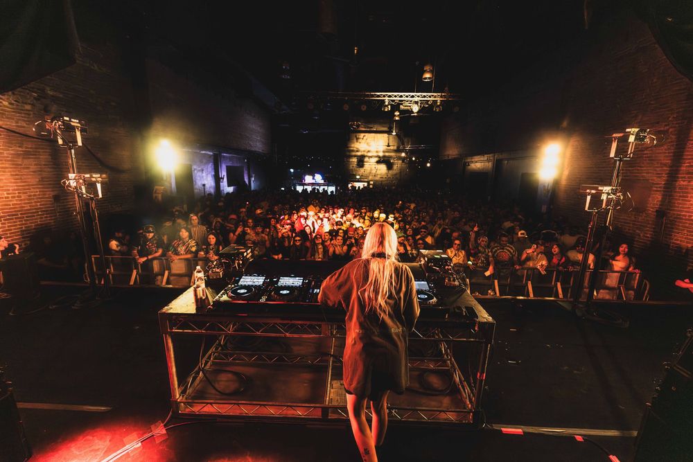 Dark concert venue with stage lights and crowd silhouettes creating atmospheric performance environment.