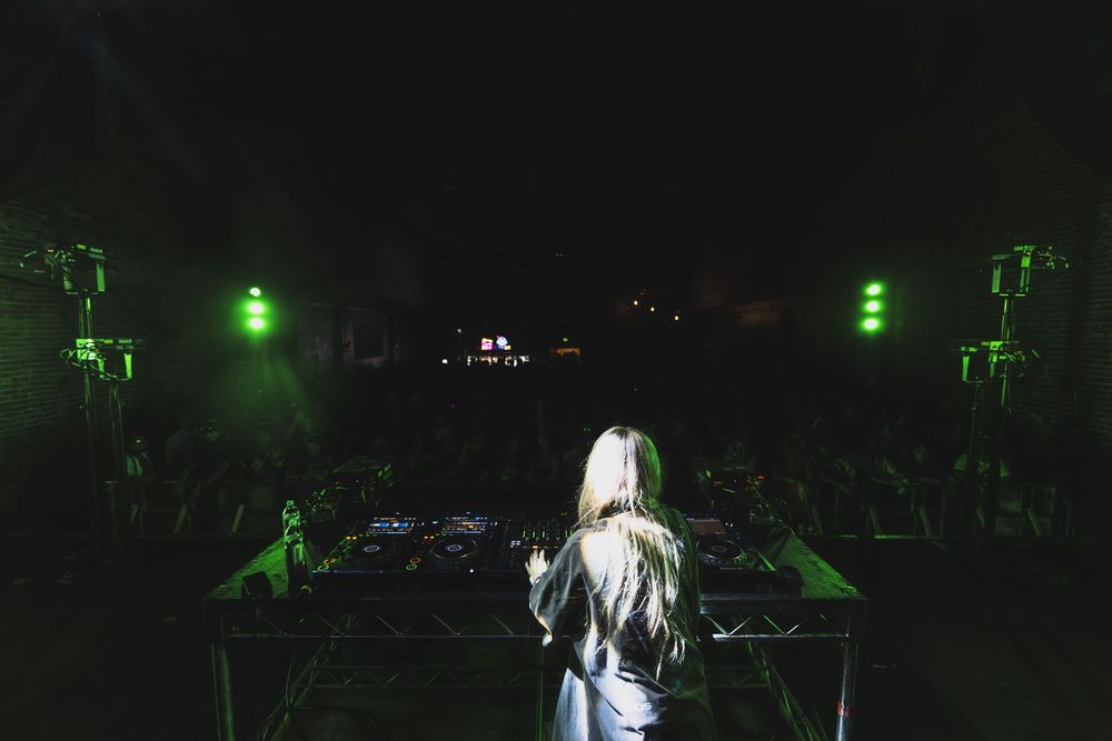Dark concert venue with performers silhouetted against green stage lights creating a dramatic atmosphere.