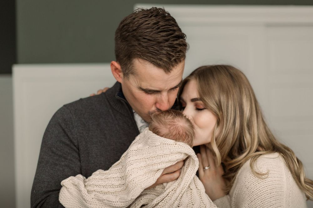 Cozy indoor engagement photos show couple sharing tender kisses while wearing casual sweaters.