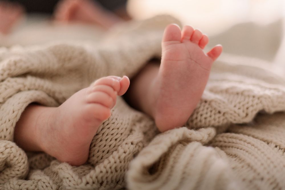 Baby's tiny feet rest on a cozy knitted blanket in warm neutral tones.