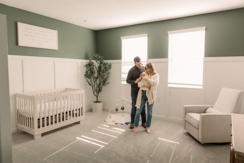 A panoramic view of a modern nursery with sage green walls, white crib, and natural light streaming through windows.