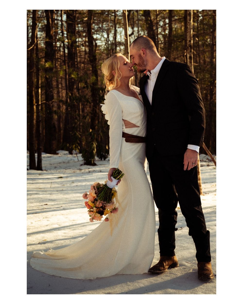 Winter wedding couple walking through snowy forest setting in formal attire.