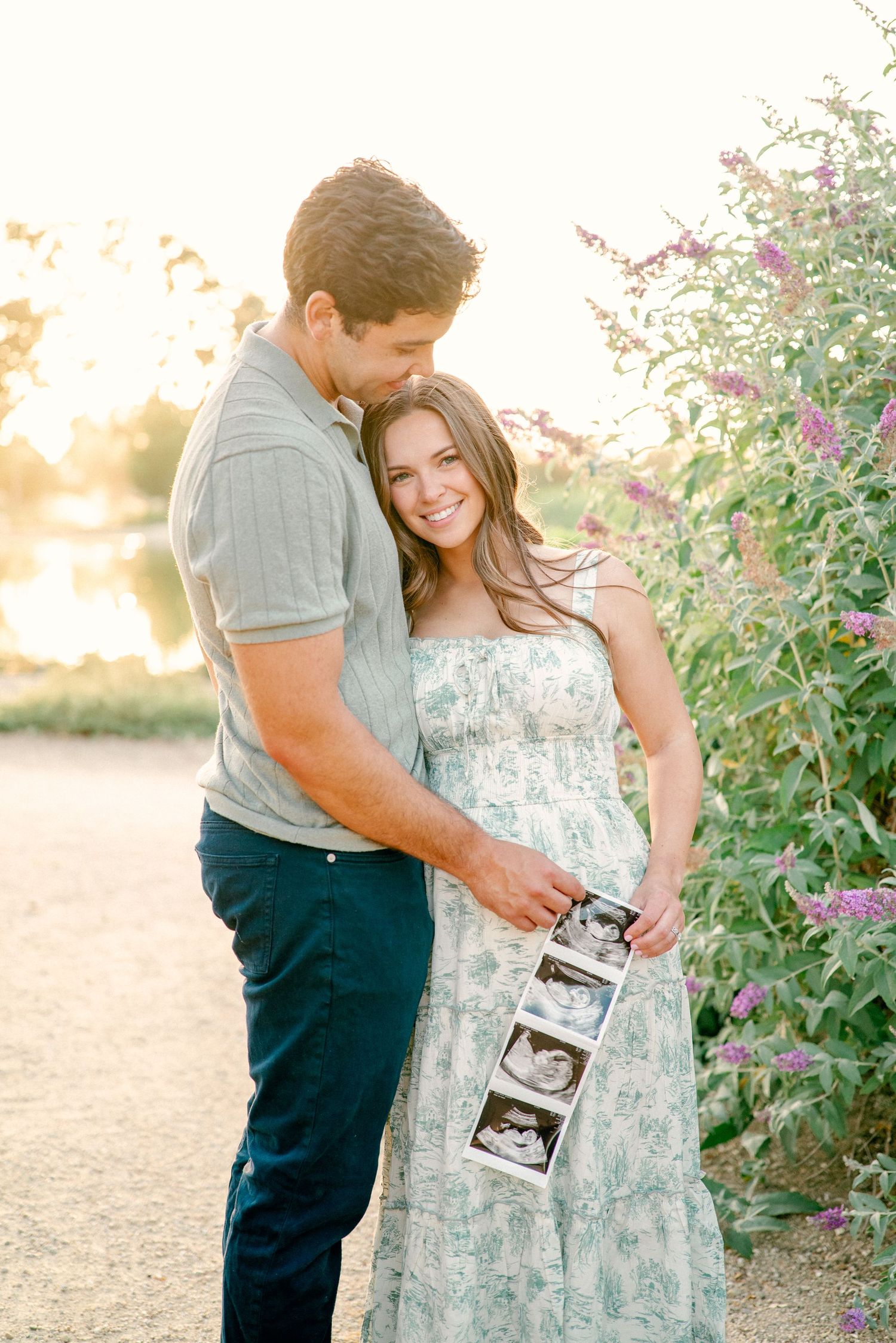 A couple in a garden setting share a tender moment while holding an ultrasound photo during a pregnancy announcement.