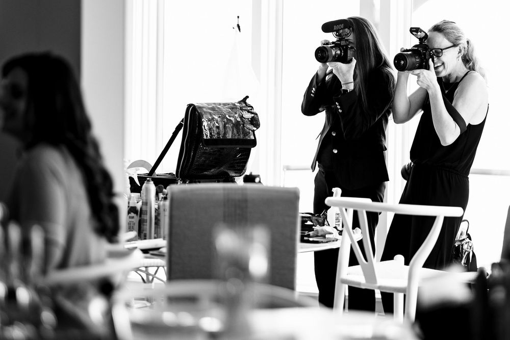 Two female photographers capturing images with professional cameras at an indoor event in black and white.