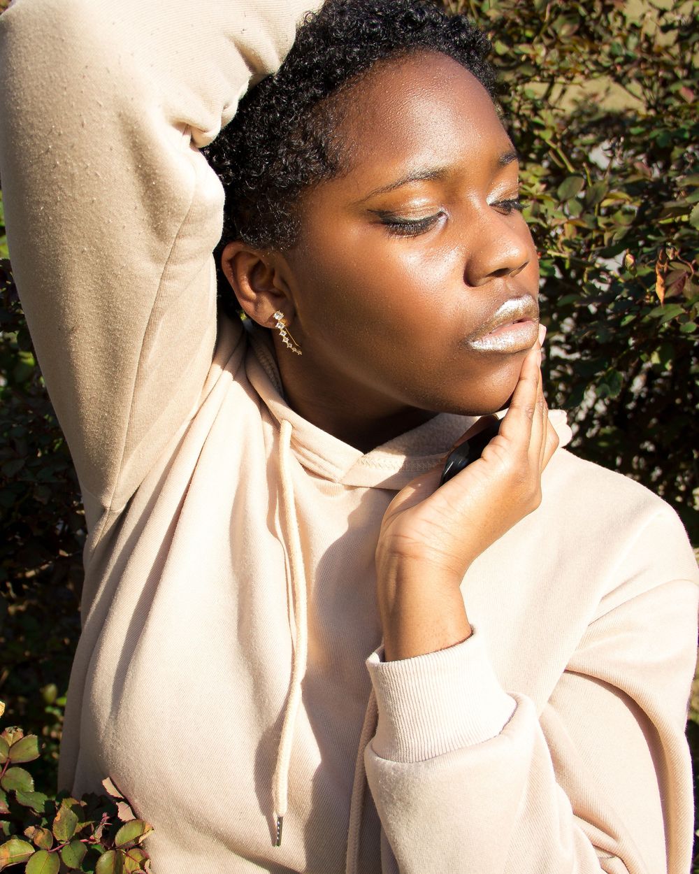 A portrait in natural sunlight shows a person in a beige sweatshort with closed eyes and glowing skin.