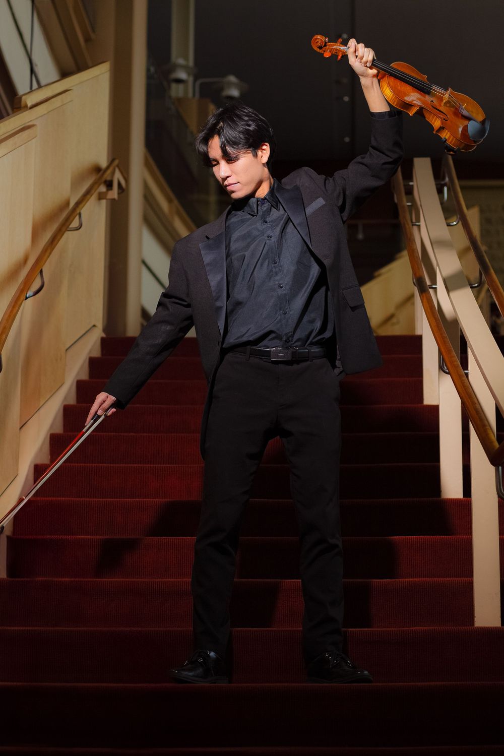 A violinist in black attire performs on carpeted stairs in a dramatic sequence of artistic poses.