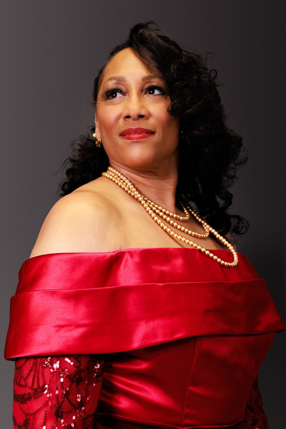 A glamorous portrait series in a red satin gown with pearl necklace against a dark background.