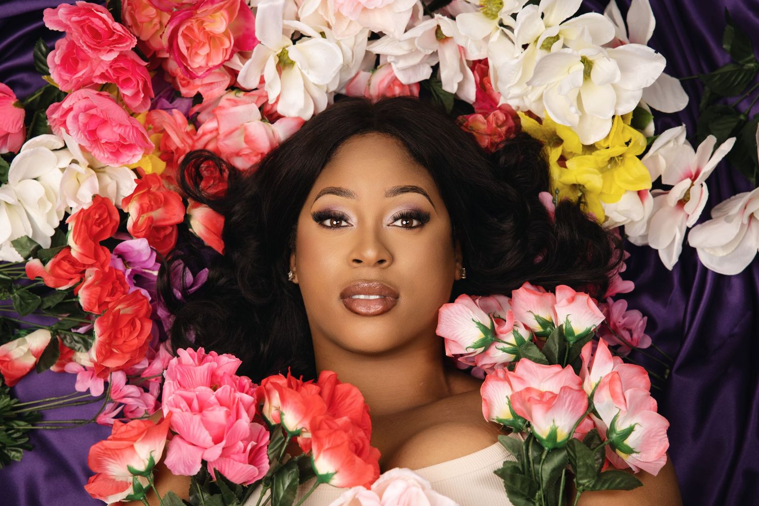 A portrait surrounded by vibrant pink, white and yellow flowers against a dark purple background.