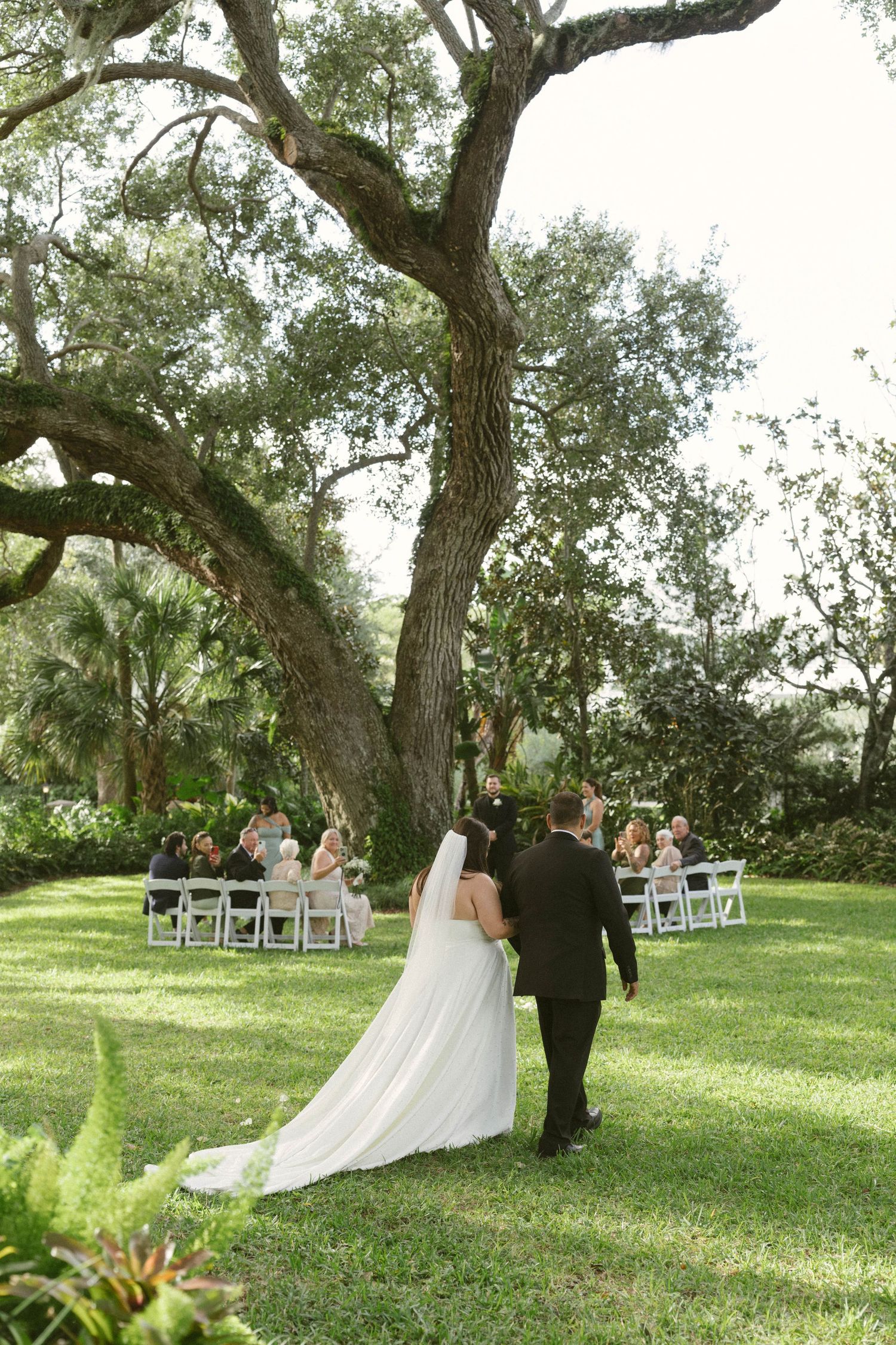Elegant wedding table decor with white floral centerpieces and wooden chairs arranged outdoors on a sunny day.