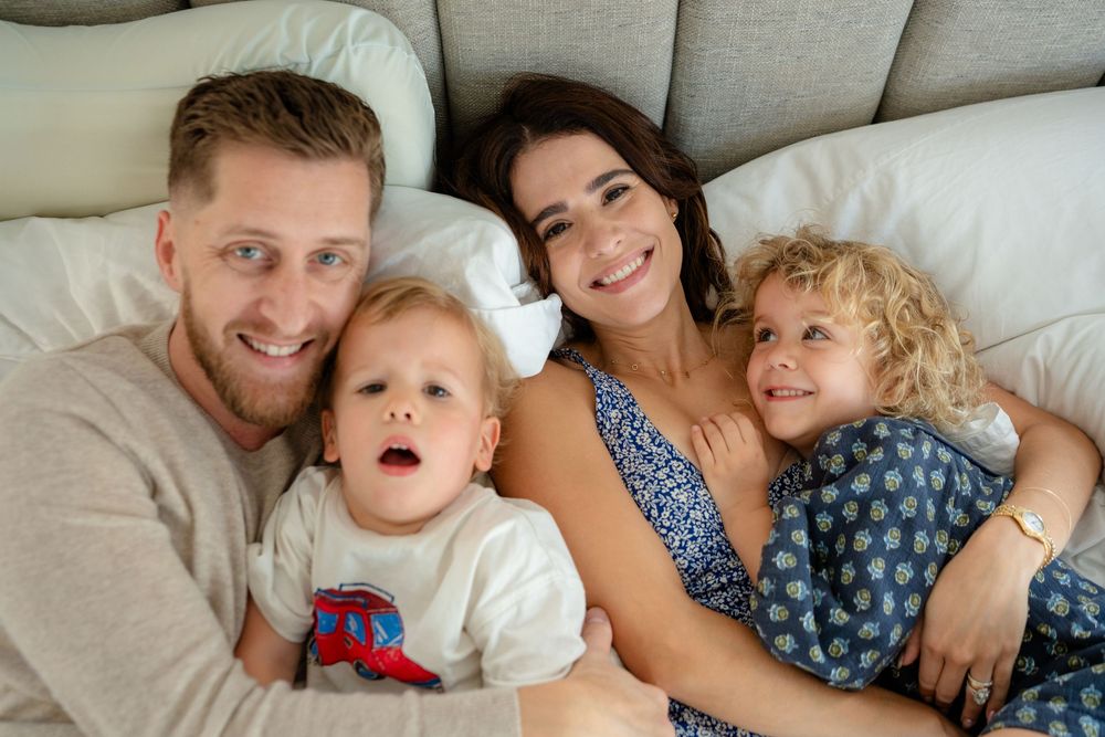 Family members lying together on white bedding while sharing tender moments and smiles.