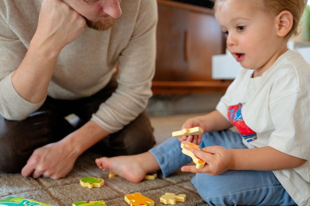 Parent and toddler playing together with colorful puzzle pieces on the floor at home.