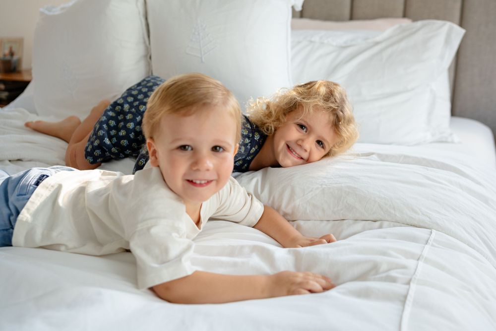 Children lying on white bedding and pillows while relaxing together during a cozy moment at home.