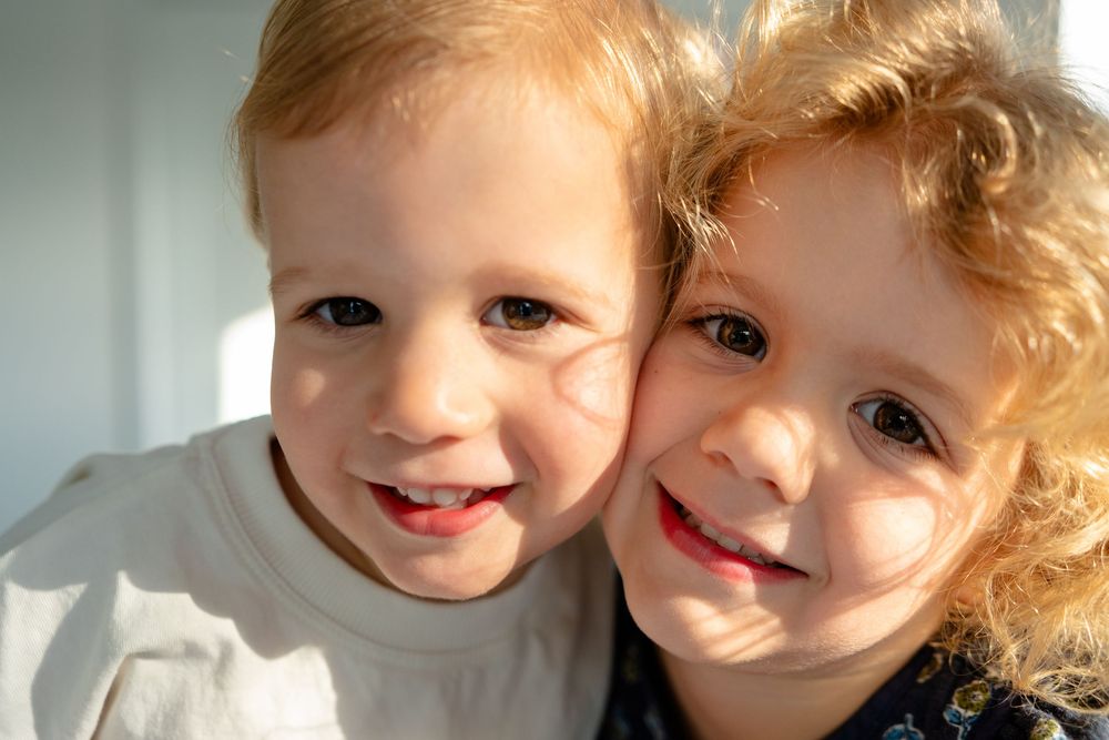 Two young children with curly hair share a joyful moment while playing together indoors.