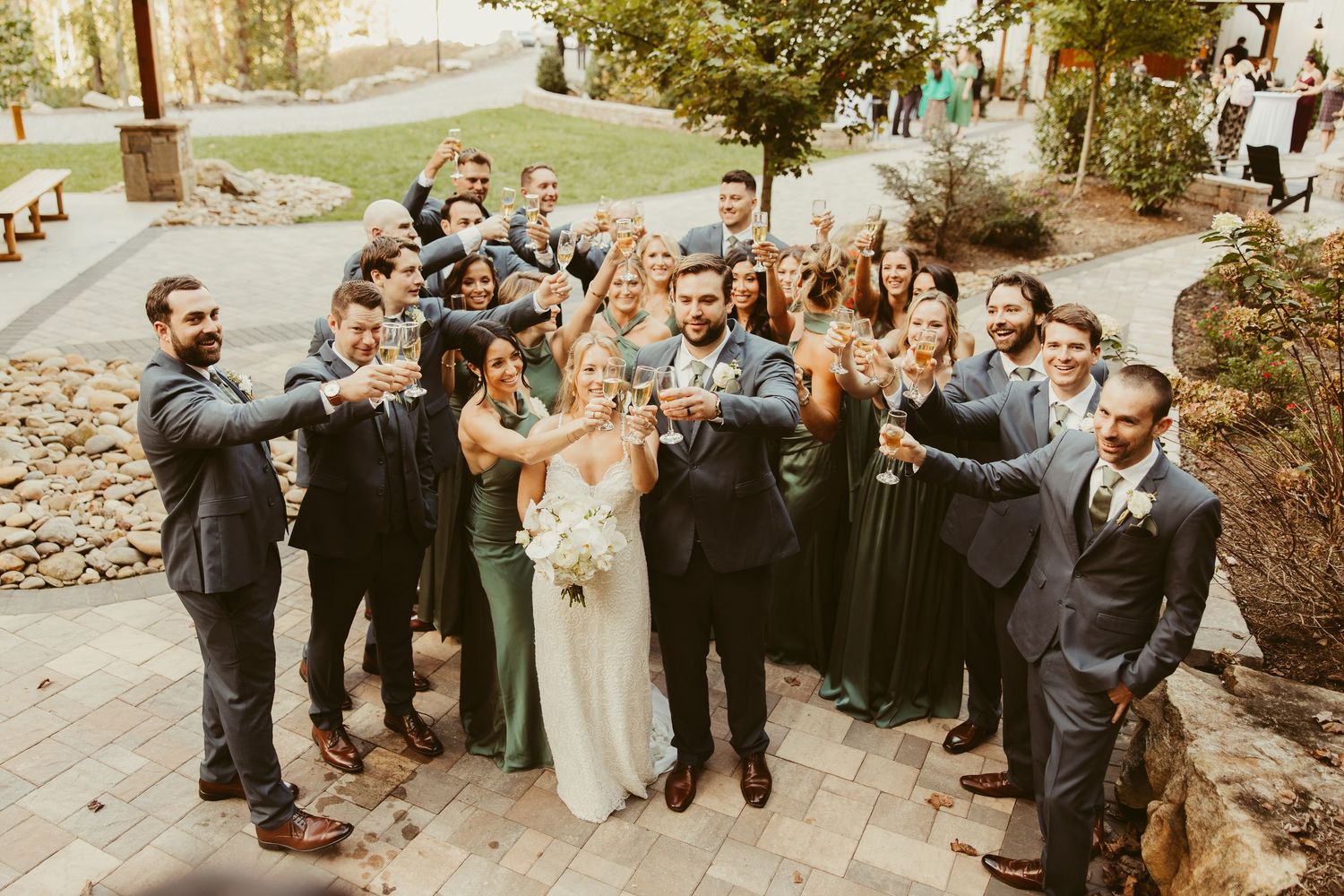 Wedding party toasting with champagne glasses outdoors at rustic venue celebration.