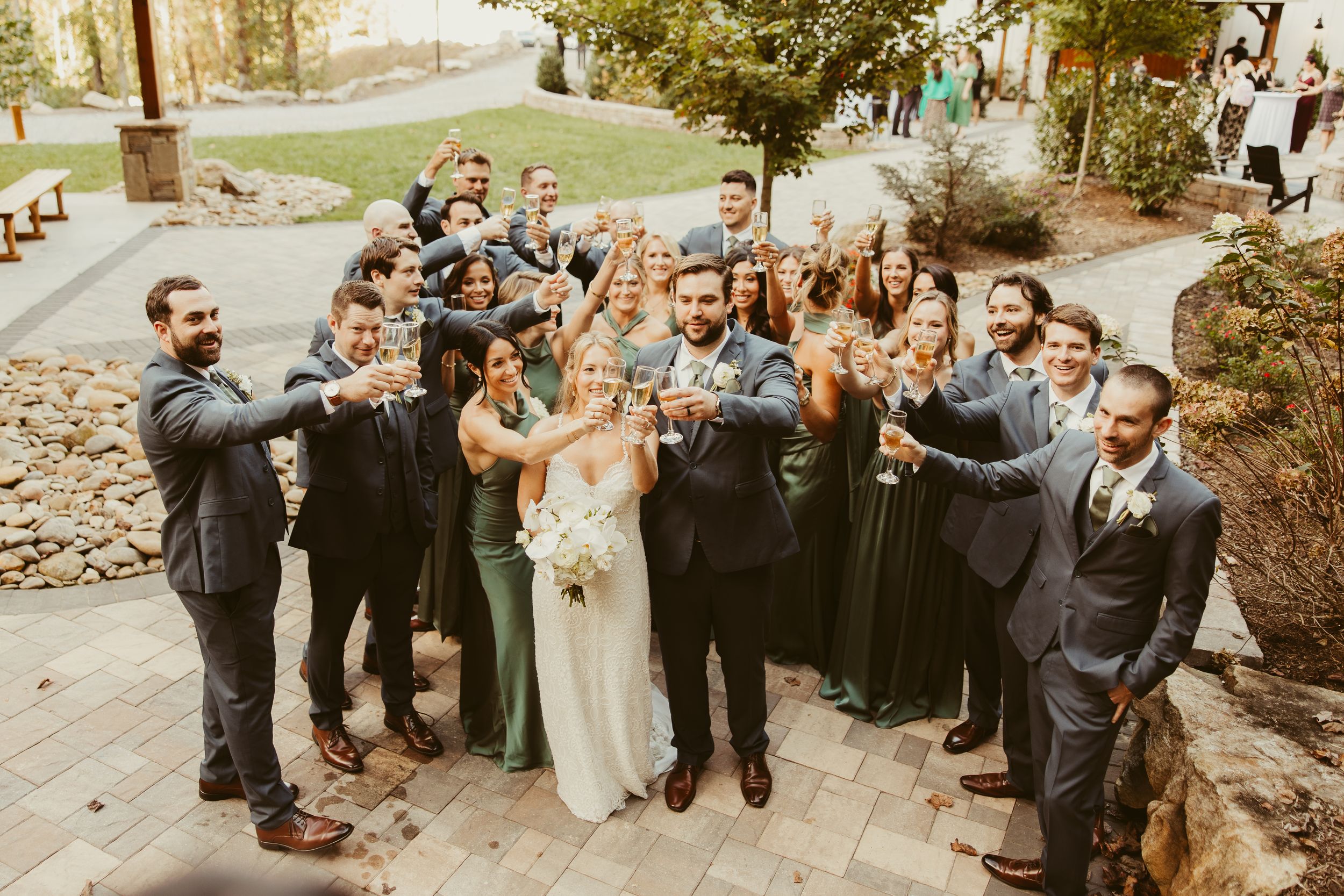 Wedding party toasting with champagne glasses outdoors at rustic venue celebration.