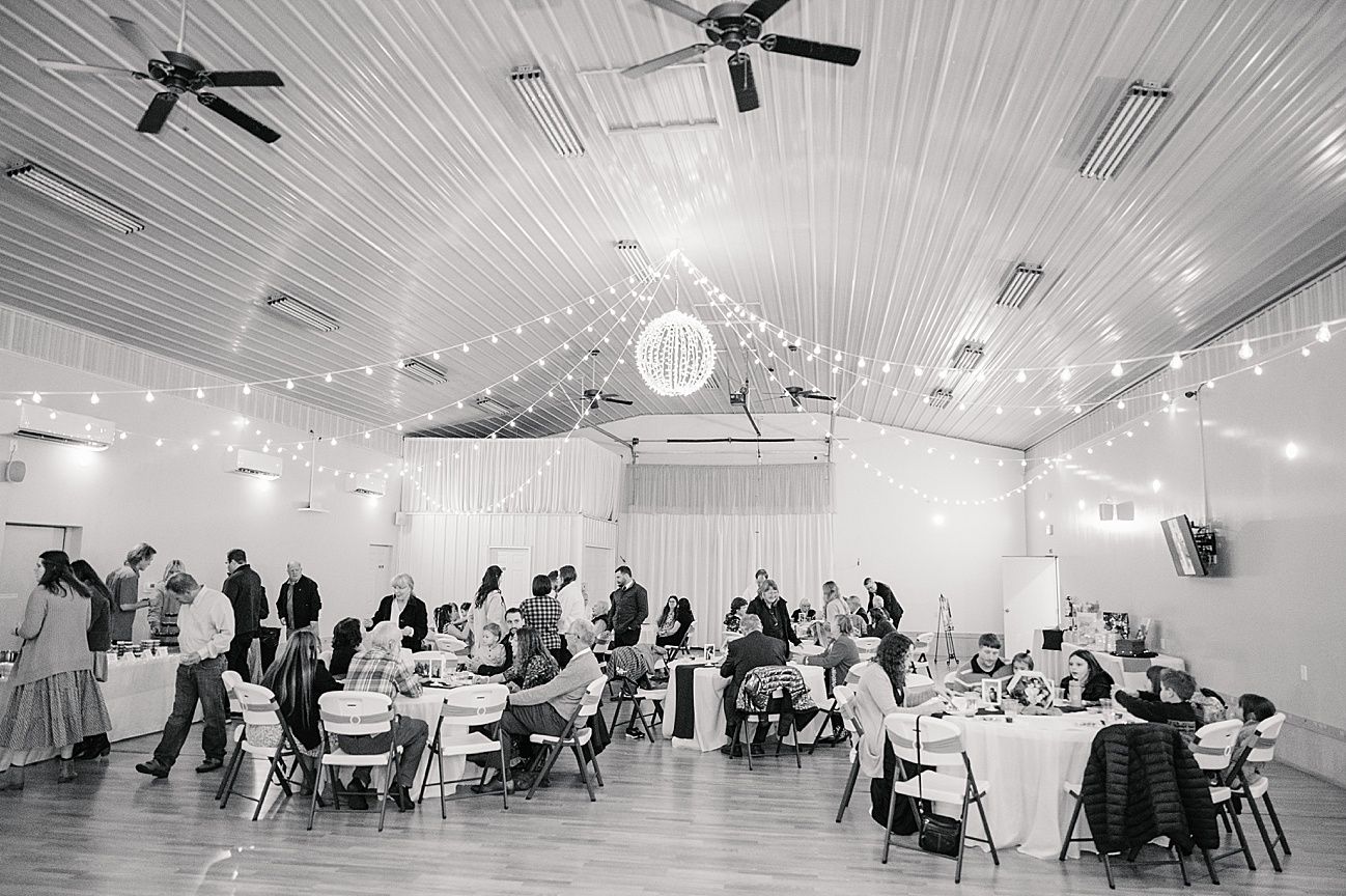 A panoramic view of a white reception hall with ceiling fans, round tables, and chairs set up for a formal event.