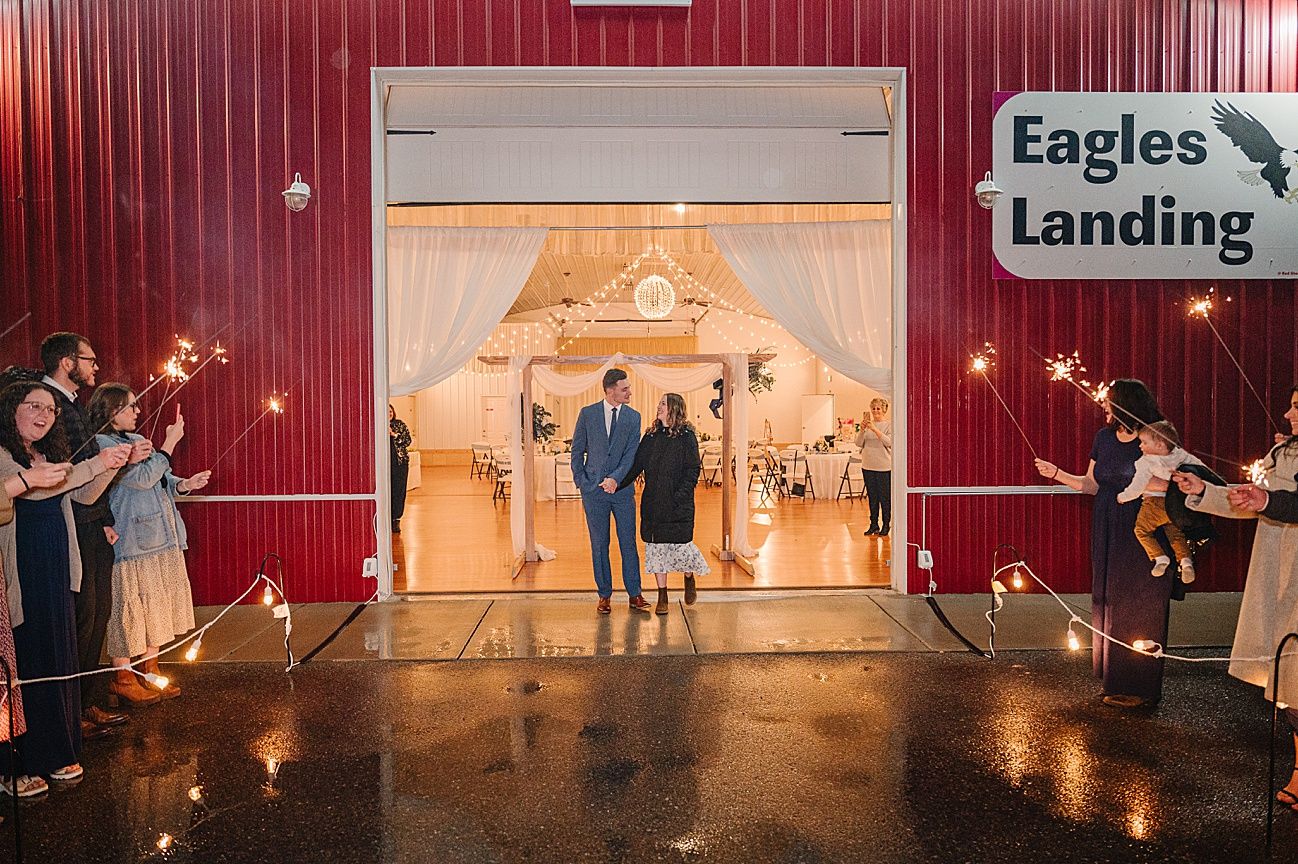 Wedding reception dance floor illuminated by warm string lights with couples dancing in a rustic barn venue.