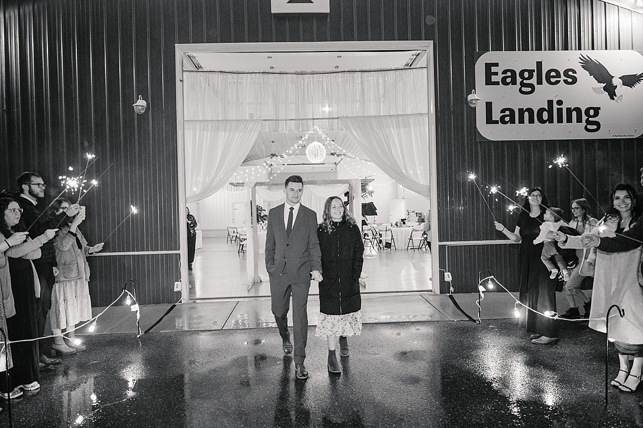 A couple exits their wedding ceremony at Eagles Landing venue while guests line the path with sparklers in black and white.