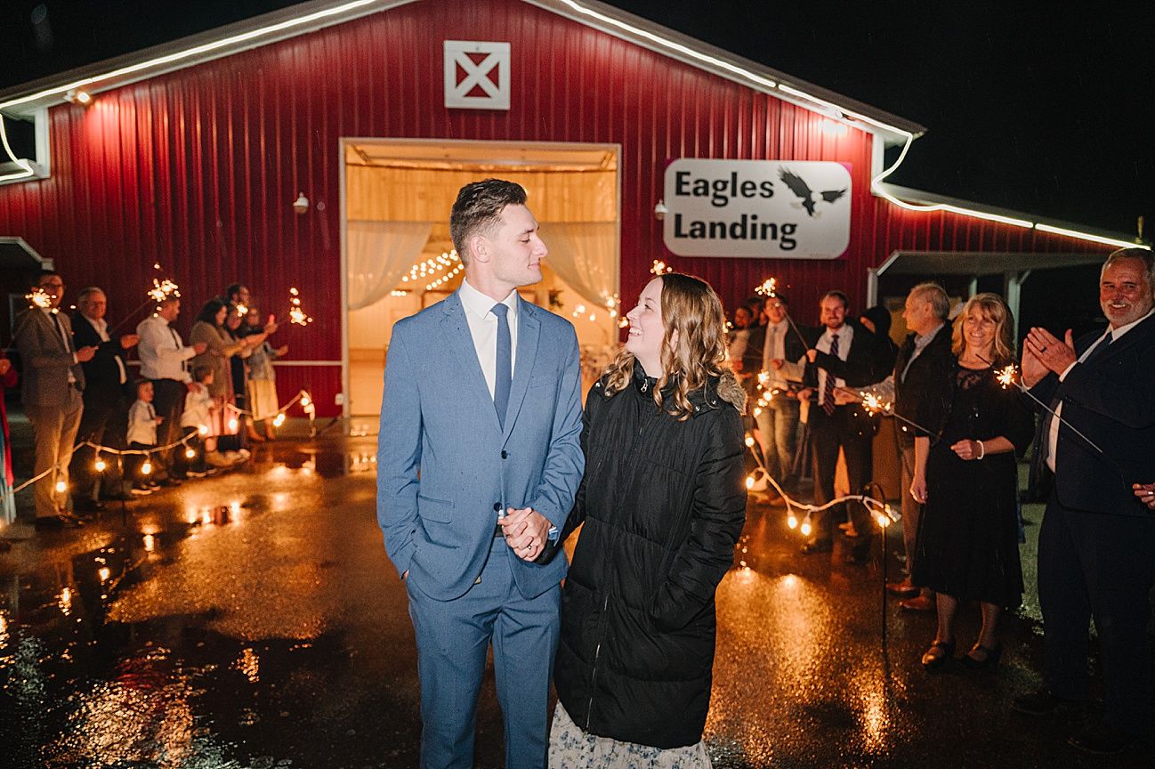 Wedding celebration at a rustic red barn venue illuminated by warm lighting at night.