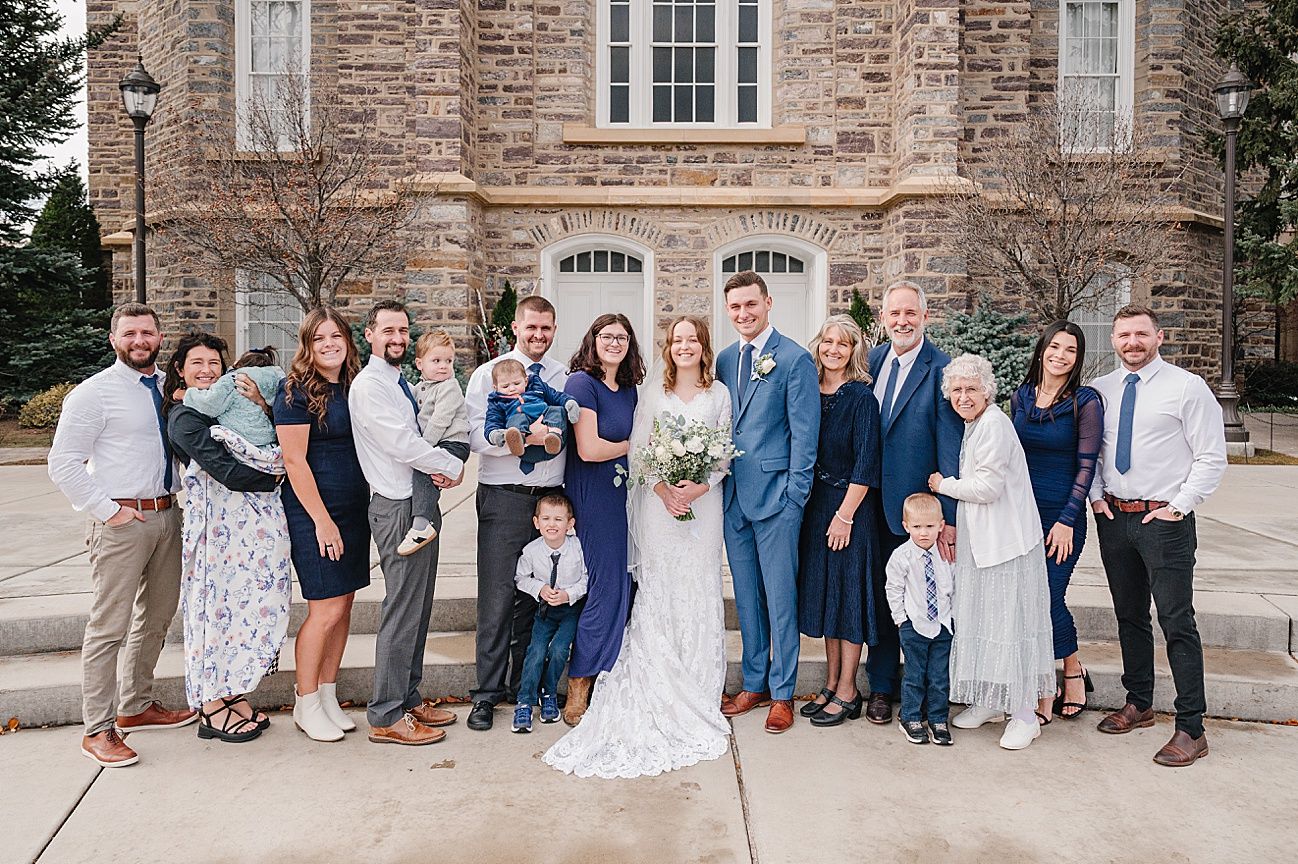 Wedding party sits on stone steps of historic church building for formal group photo.