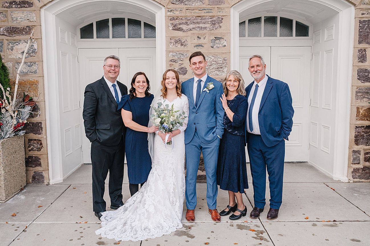 Wedding party poses in front of stone building with white garage doors in formal attire.