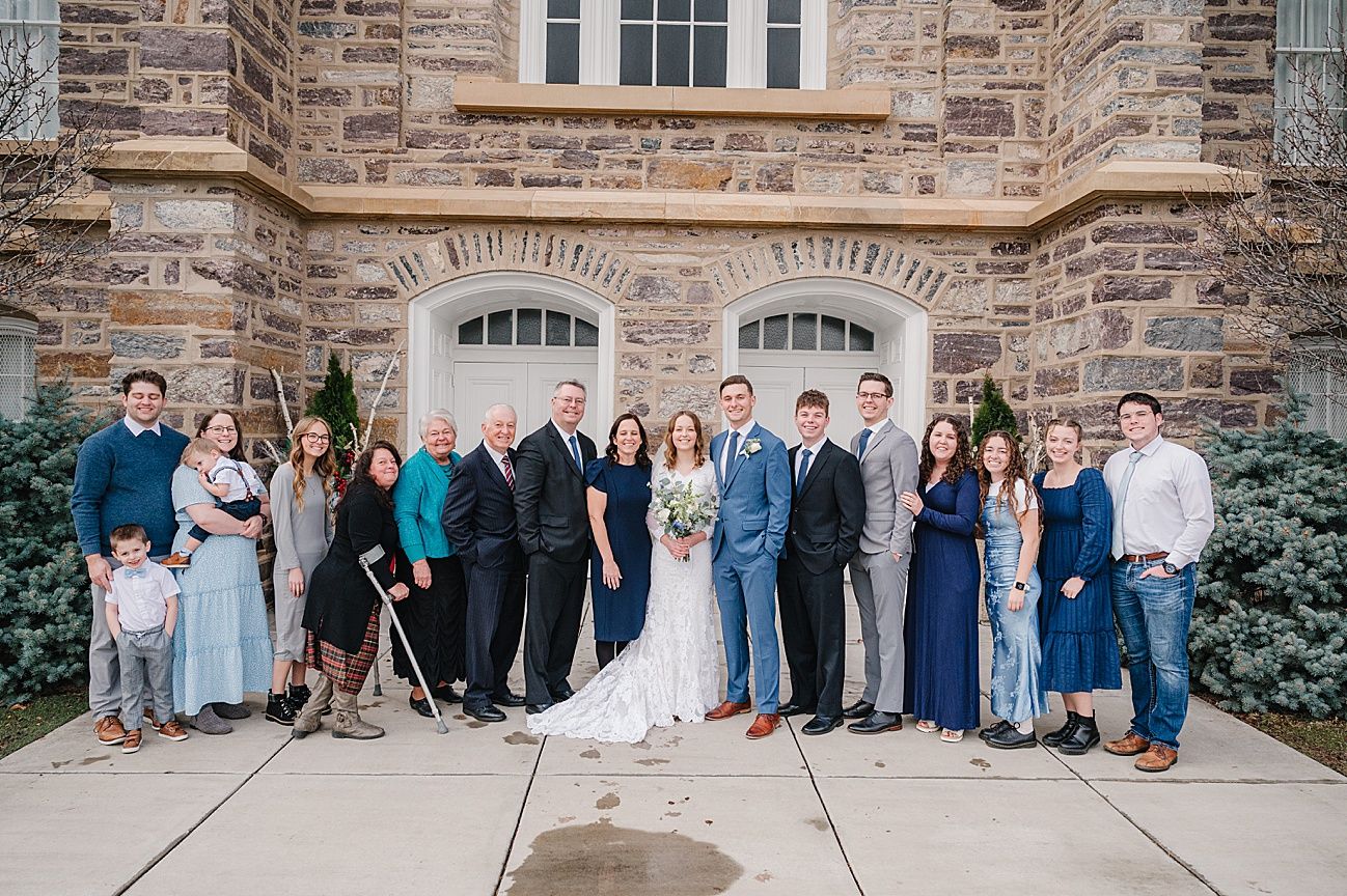 A group photo lineup against a stone building wall with light blue and gray formal attire.