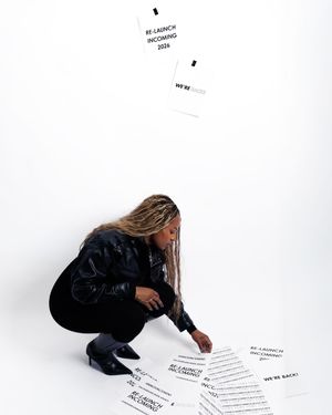 A person in dark clothing crouches down to examine papers scattered on a white floor.