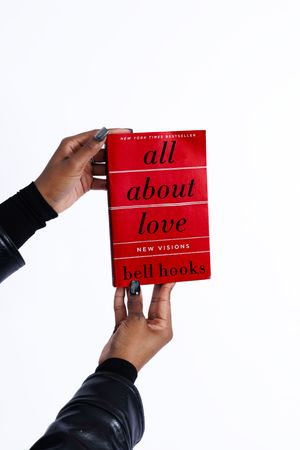 Hands holding red book titled 'All About Love' by bell hooks against white background.
