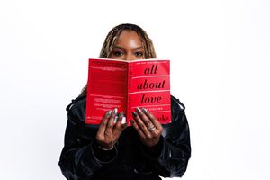 Someone holds up a red book in front of their face while wearing a black jacket against a white background.