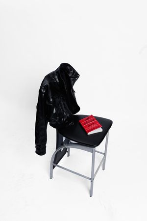 A black leather jacket draped over a white chair shown from three different angles in a minimalist setting.