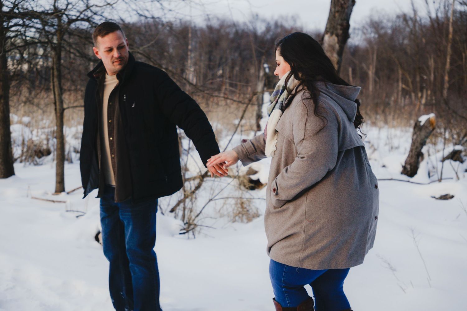 A couple holding hands and walking together through a snowy landscape during a winter outdoor couples session.