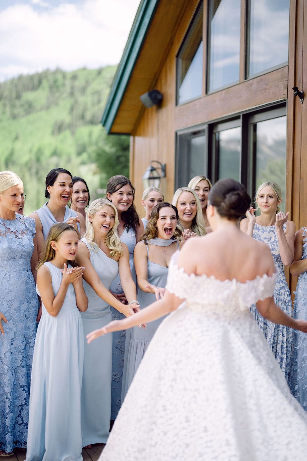 Bridesmaids in light blue dresses react with joy and surprise as they see the bride in her white wedding gown.